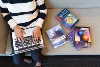 A person learning how to program using a laptop and books